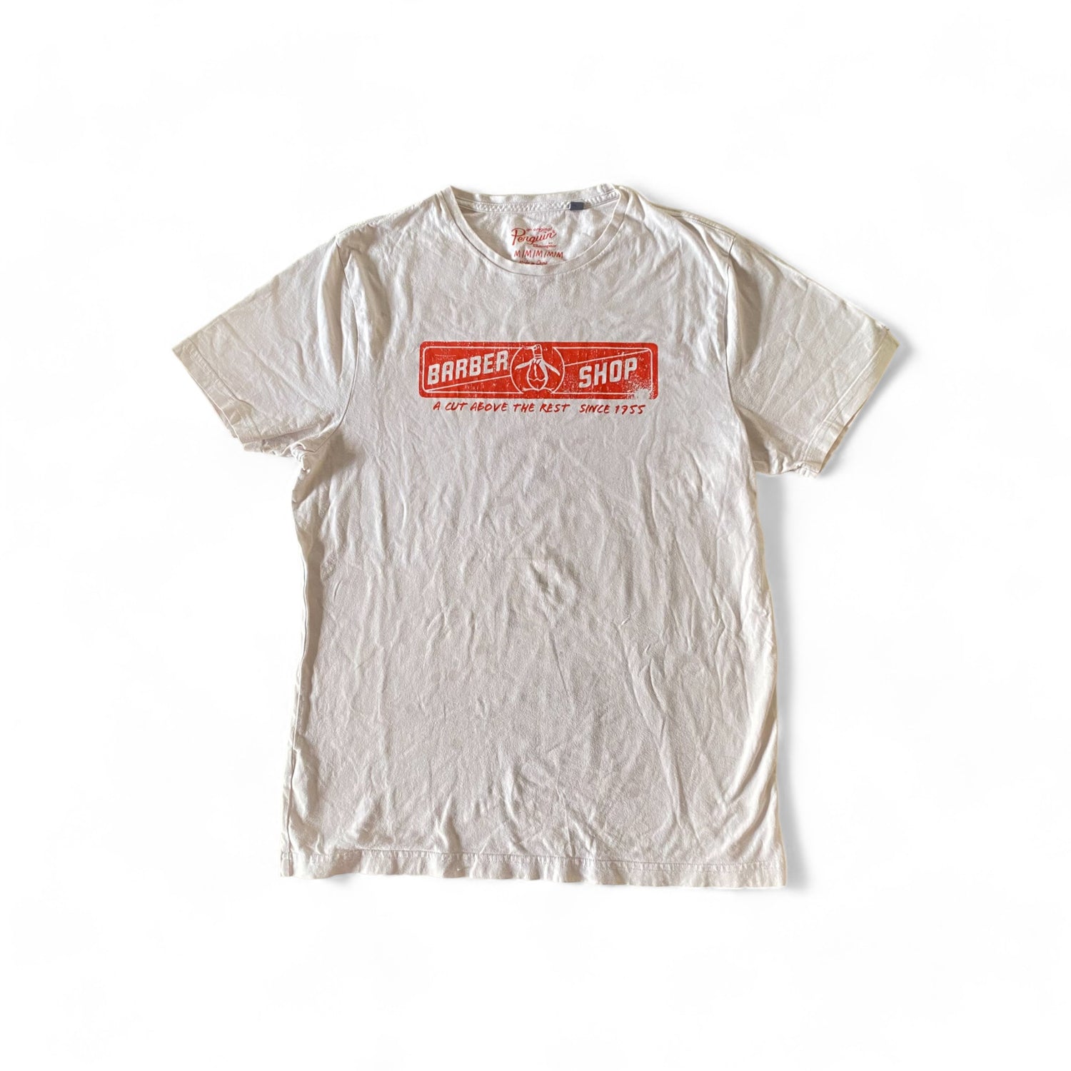 White crewneck t-shirt with a red barber shop logo on the chest. The text “BARBER SHOP” is written above the logo, and “A CUT ABOVE THE REST SINCE 1955” is written below it.  Google vintage and second hand clothing